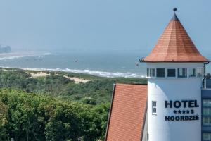a hotel with a clock tower next to the ocean at Noordzee, Hotel & Spa in Cadzand-Bad