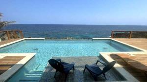 een zwembad met twee stoelen en de oceaan bij Casa Flomingo Roatan in West Bay