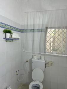 a white bathroom with a toilet and a window at Tabasamu Gardens in Diani Beach
