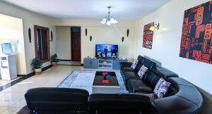 a living room with a black leather couch and a tv at Tribal Themed 3BR Penthouse in Nairobi