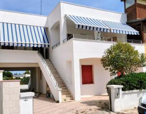 una casa bianca con tende da sole a strisce blu e bianche di Appartamenti Alba e Tramonto a Marina di Mancaversa