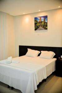 hotel quatro coracoes في أرابيراكا: غرفة نوم مع سرير أبيض كبير مع صورة على الحائط