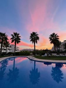 a sunset over a swimming pool with palm trees at Hestía Vera Salinas Tu hogar para desconectar in Playas de Vera