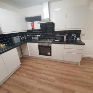 a kitchen with white cabinets and black tiles on the wall at Beautiful place near Dagenham East Station in Dagenham