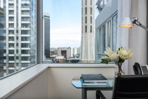 a room with a desk and a window with a table with books at Rydges Auckland in Auckland