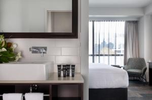 a bathroom with a sink and a bed and a mirror at Rydges Auckland in Auckland