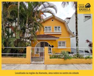 uma casa amarela com uma cerca e palmeiras em Casa Amarela Blumenau Hospedagem Alternativa em Blumenau