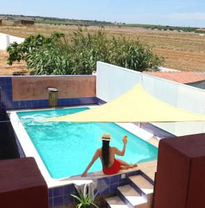 une femme dans un chapeau assise dans une piscine dans l'établissement Aladin Comfort Country House, à Campinho