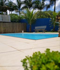 a swimming pool with a bench and palm trees at Pousada Recanto Rainha do Lago in Capitólio
