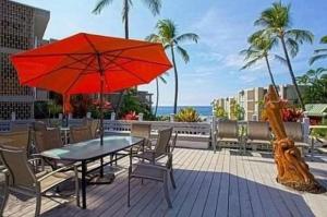 a table and chairs with a red umbrella on a deck at Enjoy the sunset at OCEAN FRONT 1BR Apartment - pool on site! in Kailua-Kona