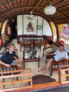 twee mannen zitten in stoelen in een kamer met tafels bij Thara's Houseboat in Alleppey