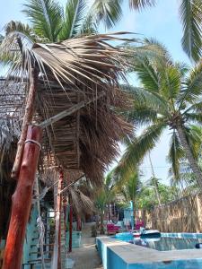 una cabaña de paja junto a una piscina con palmeras en El Puente en El Paredón Buena Vista