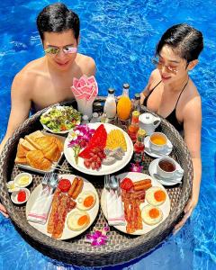 Club Bamboo Boutique Patong Beach Resort في شاطيء باتونغ: رجل وامرأة يجلسان في مسبح مع صينية طعام
