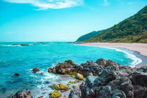 a beach with rocks and blue water and mountains at Casa temporada próximo à parque in Penha