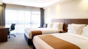 a hotel room with two beds and a desk at Holiday Inn Auckland Airport, an IHG Hotel in Auckland