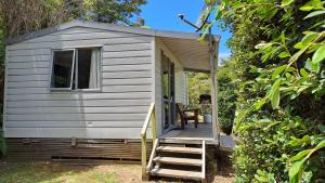 a tiny house with a porch and a staircase at Whatuwhiwhi TOP 10 Holiday Park in Tokerau Beach