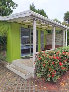 Whatuwhiwhi TOP 10 Holiday Park في Tokerau Beach: منزل أخضر صغير مع شرفة وزهور