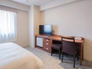 Vessel Hotel Miyakonojo في مياكونوجو: غرفة نوم مع مكتب مع تلفزيون وسرير