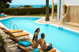 a man and woman sitting on lounge chairs in a swimming pool at Iberostar Selection Andalucia Playa in Chiclana de la Frontera