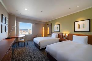 a hotel room with two beds and a desk at Hotel Associa Toyohashi in Toyohashi