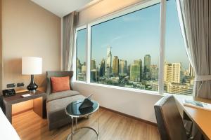 a room with a chair and a desk and a large window at Eastin Grand Hotel Sathorn in Bangkok