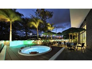Green Rich Hotel Okinawa Nago - Vacation STAY 49889v في ناغُو: حوض استحمام ساخن على السطح مع طاولات ومظلات