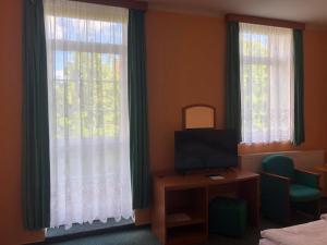 Zimmer mit 2 Fenstern, einem TV und einem Schreibtisch. in der Unterkunft Grandhotel Nový Bor in Nový Bor