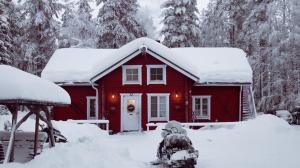 une maison rouge avec de la neige sur le toit dans l'établissement Kotatuli Forest Lodge, à Rovaniemi