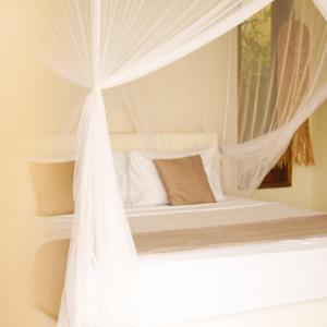 Cama blanca con dosel y cortinas blancas en Kini Resort - Oceanfront Bamboo Eco Lodges, en Sekongkang