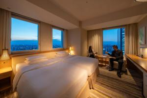 a hotel room with a large bed and two people sitting at a table at Nagoya JR Gate Tower Hotel in Nagoya