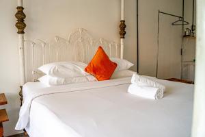 Cama blanca con almohada naranja y almohadas blancas en Sepeda Hostel, en Canggu