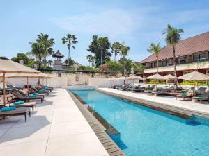 una piscina en el complejo con tumbonas y sombrillas en Novotel Bali Benoa en Nusa Dua