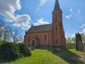 an old brick church with a steeple on a grass field at Ferienwohnung 2 Am Rodelberg in Priborn