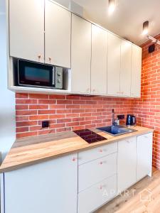 a kitchen with white cabinets and a brick wall at Biskupia Central Apartment in Gdańsk