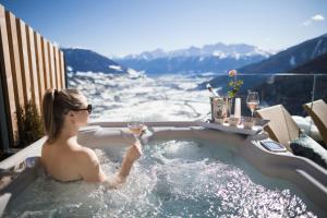 DAS GERSTL Alpine Retreat في ماليس فينوستا: امرأة في حوض استحمام ساخن مع كوب من النبيذ