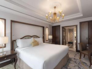 - une chambre avec un grand lit blanc et un lustre dans l'établissement Raffles Makkah Palace, à La Mecque