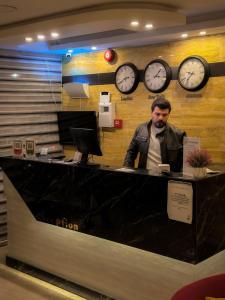 a man sitting at a counter with clocks on the wall at Petra Corner Hotel in Wadi Musa