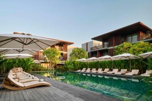 einen Pool mit Stühlen und Sonnenschirmen neben einem Gebäude in der Unterkunft Andaz Pattaya Jomtien Beach, a Concept by Hyatt in Na Jomtien
