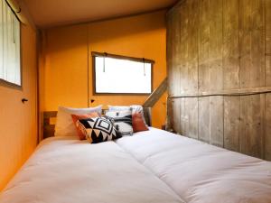 een groot wit bed in een kamer met oranje muren bij Glamping met bar en privé sanitair voor 5 Personen Sneezy in Behelp