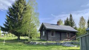 a small wooden house in a field with a tree at Log Cabin from 1820s with wood-heated sauna in Hassela