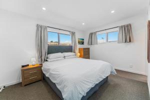 a white bedroom with a bed and two windows at Motuoapa Getaway - Lake Taupo Holiday Home in Turangi
