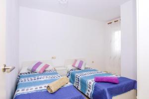 two beds in a white room with purple and pink pillows at La Puntica in Carboneras