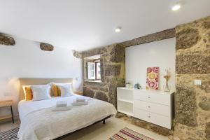 a bedroom with a king sized bed and a stone wall at Quinta Rolim do Bouro By Sé Apartamentos in Roucio