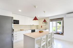 a kitchen with white cabinets and a kitchen island with white chairs at Quinta Rolim do Bouro By Sé Apartamentos in Roucio