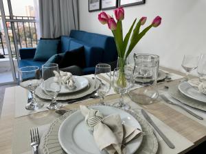 a dining room table with plates and glasses and pink tulips at Apartamento novo decorado com sacada e linda vista da Cidade in Sao Paulo