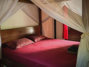 ein Schlafzimmer mit einem Himmelbett mit einer roten Bettdecke in der Unterkunft Little Bear Bungalows in Gili Air