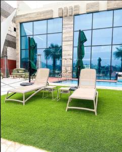 zwei Stühle und ein Tisch auf Gras neben einem Pool in der Unterkunft X Beach House in Al Khīrān