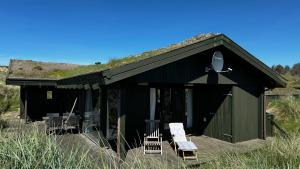 Un edificio negro con sillas y techo de hierba. en Veludstyret sommerhus i unik natur 350 m fra lækker badestrand - helårsbolig, en Saltum