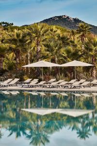 a pool with chairs and umbrellas and palm trees at Les Prairies de la Mer in Grimaud