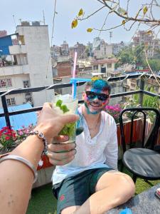 Ein Mann mit einem gemalten Gesicht, der einen Drink hält. in der Unterkunft Yog Hostel in Kathmandu